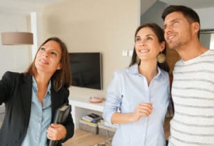 Image d'illustration représentant un promoteur immobilier montrant les détails d'un salon d'une maison à un couple souriant