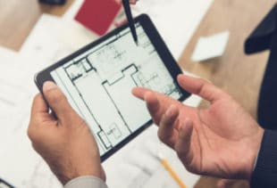 Image d'illustration représentant un homme debout tenant une tablette tactile avec un plan d'appartement et montrant le bleu