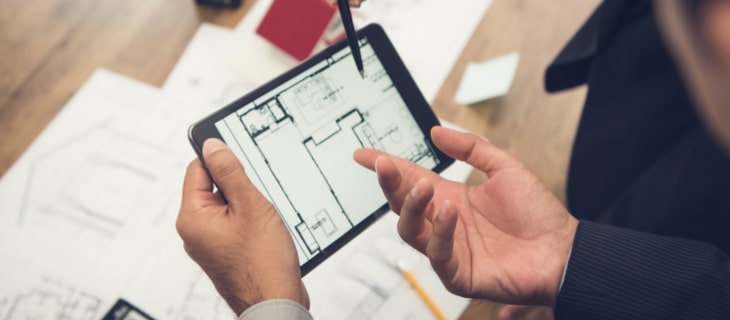 Image d'illustration représentant un homme debout tenant une tablette tactile avec un plan d'appartement et montrant le bleu