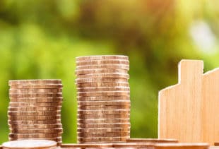 Image d'illustration représentant des empilements de pièces de monnaie et une petite maison en bois