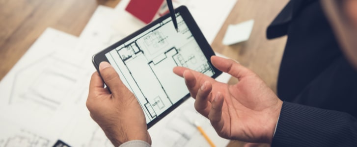 Image d'illustration représentant un homme debout tenant une tablette tactile avec un plan d'appartement et montrant le bleu